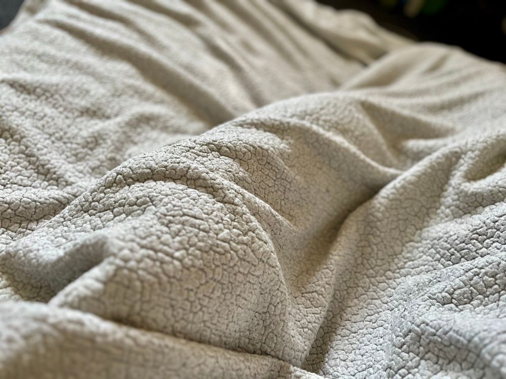 A white fuzzy blanket with a large lump—there’s a cat snoozing under it!