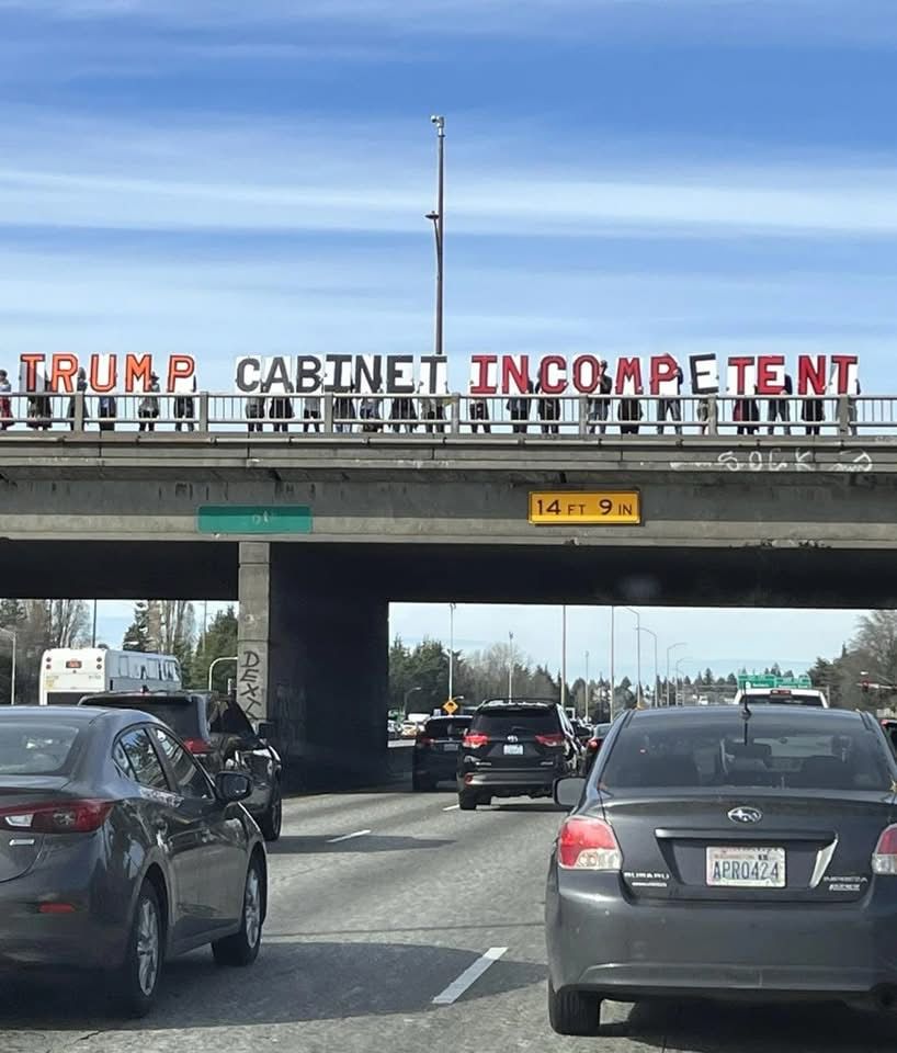 Large banner over a freeway, text reads “ TRUMP
CABINET INCOMPETENT” 