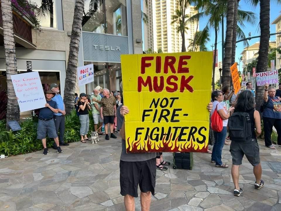 Protest sign:  “FIRE MUSK
NOT FIRE-FIGHTERS”