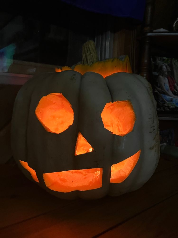 The pumpkin, now carved and sporting a cute silly expression, glowing from real candle light.