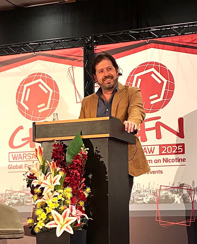 Jacob Grier stands on stage at a speaker podium, smiling while delivering his keynote address at the 2025 Global Forum on Nicotine in Warsaw.