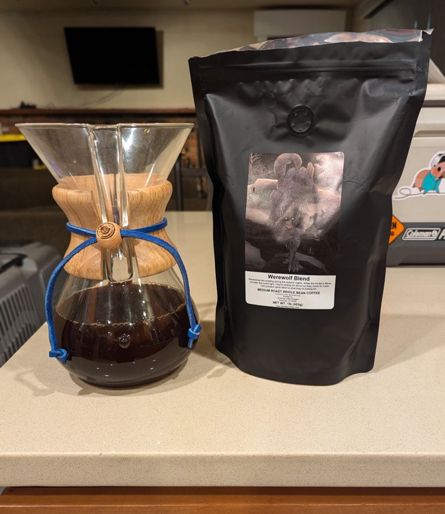A chemex coffee maker with coffee in it. It's next to a black coffee bag with a label that has an illustrated werewolf on it. The coffee is "Werewolf Blend."
