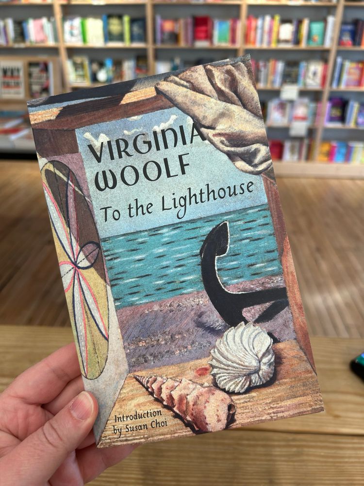 Holding up a UK cover of To The Lighthouse by Woolf with an ocean, anchor and shells on the cover