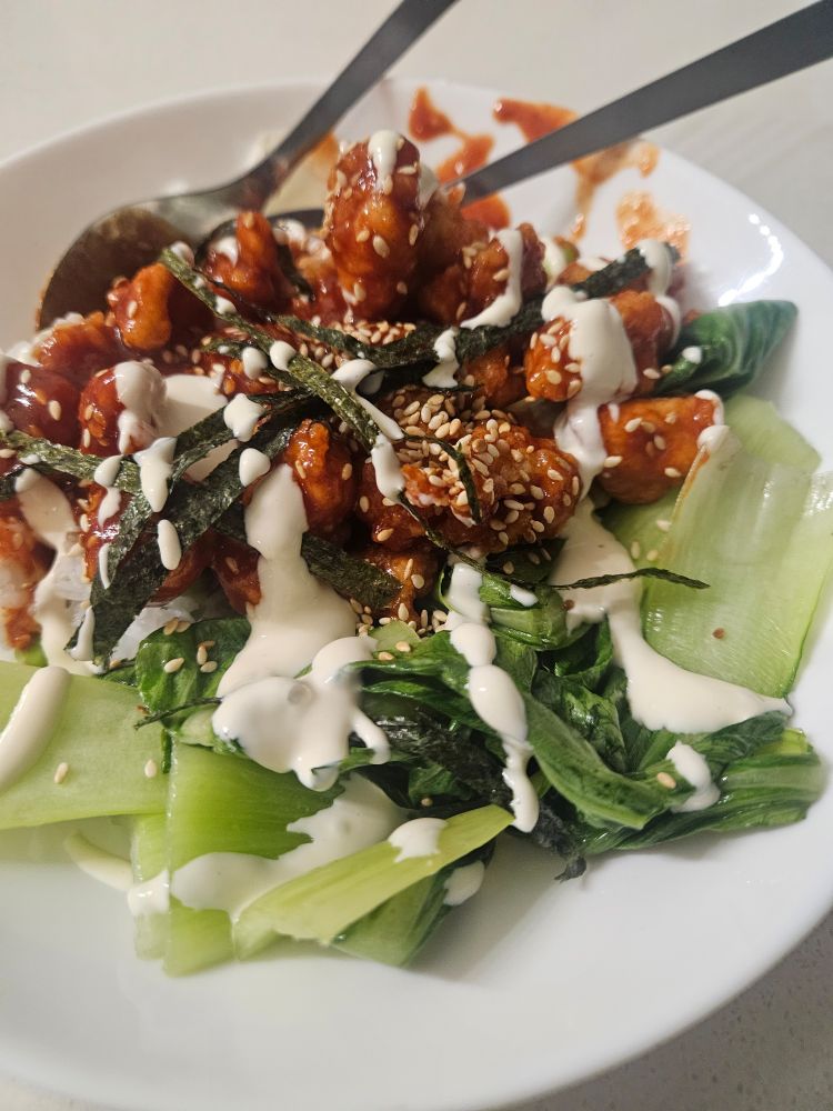 A plate of pak choi, rice and Korean fried chicken, topped with toasted sesame seeds. 