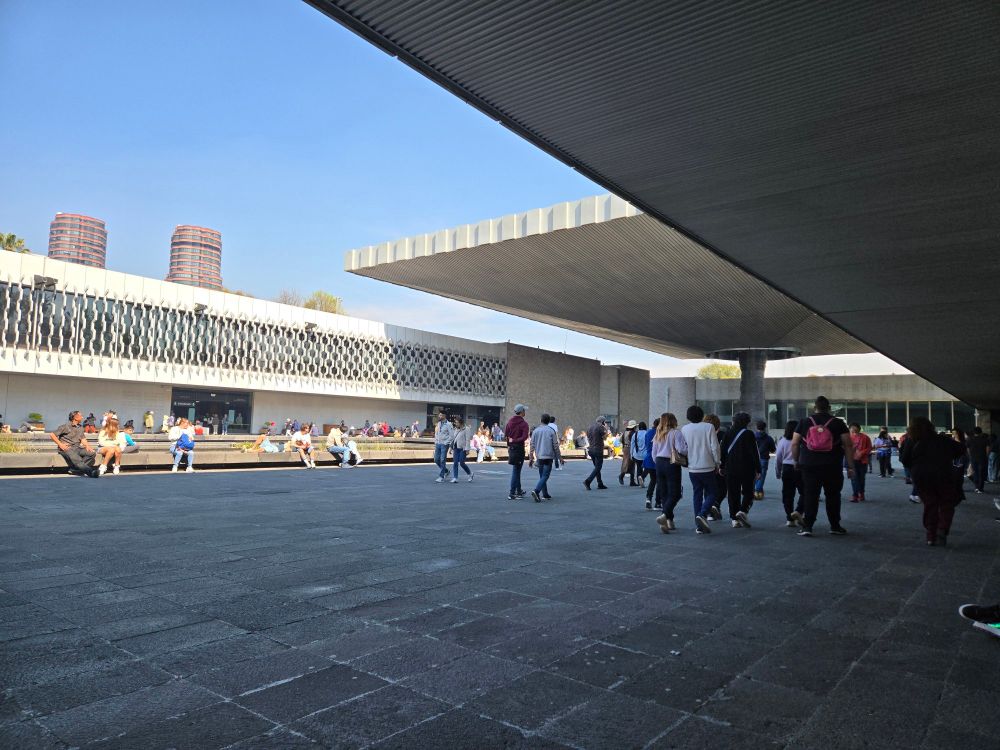 Large courtyard with a free standing canopy with waterfall in the center. Sunny day with skyscrapers in the distance. 