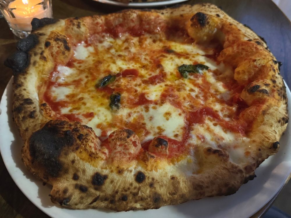 Photo of a Neapolitan style margherita pizza, a huge fluffy crust surrounds an interior of melted mozzarella and red sauce.