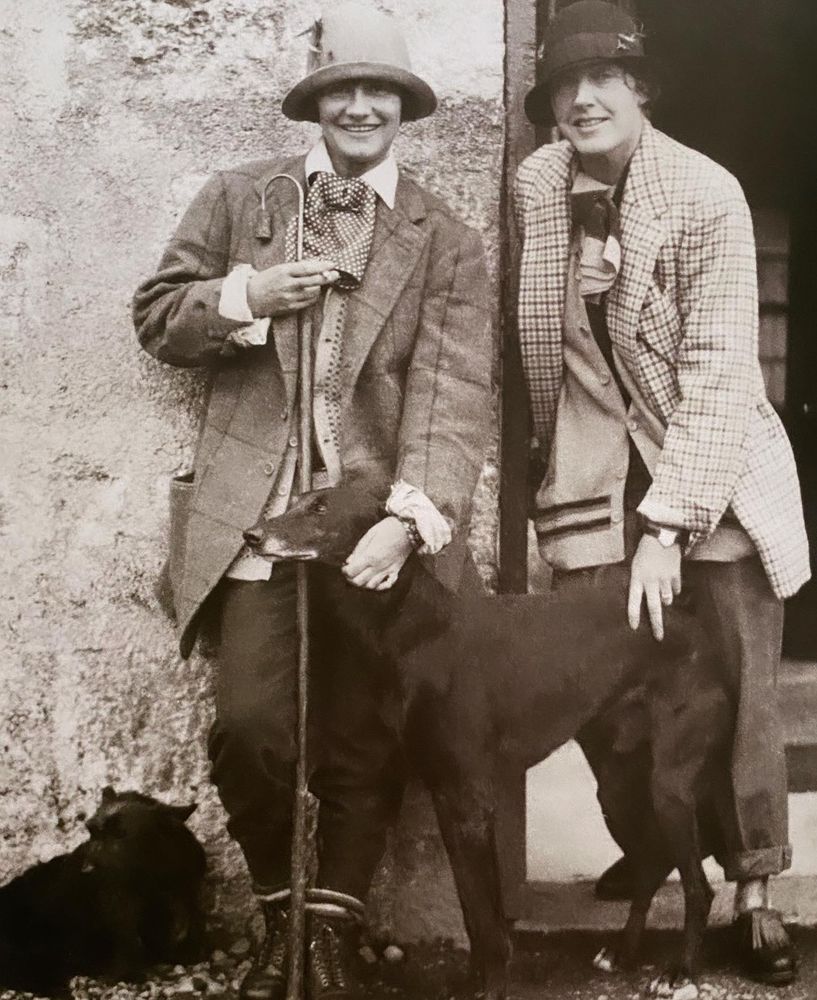 Photo of two women (one Chanel) wearing oversized tweed blazers, large cravats and petting a dog.