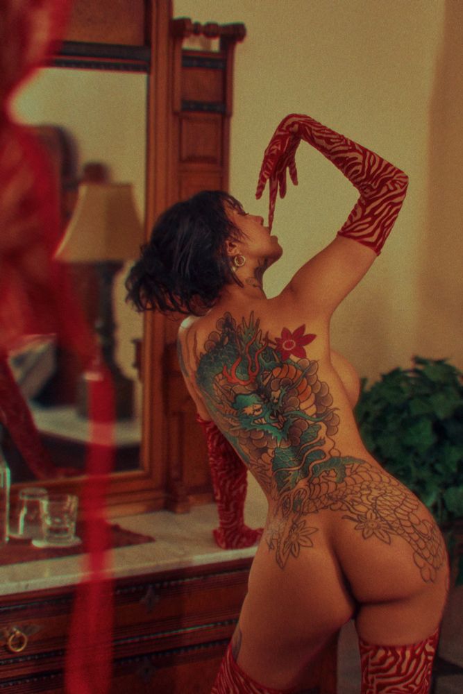 Up three flights of stairs, in a decadent victorian home turned airbnb, waits Ravyn Alexa. She has already anticpated your needs and has begun to remove her red tiger stripped lingerie. Her round ass cuts into her thin waist, inviting your hands to grab her. Her heavy tits taunt you with only a glimpse of their round edges, as she turns to slip off her gloves with her teeth. She is a vision of the goddess in the soft yellow light of the chandelier. 