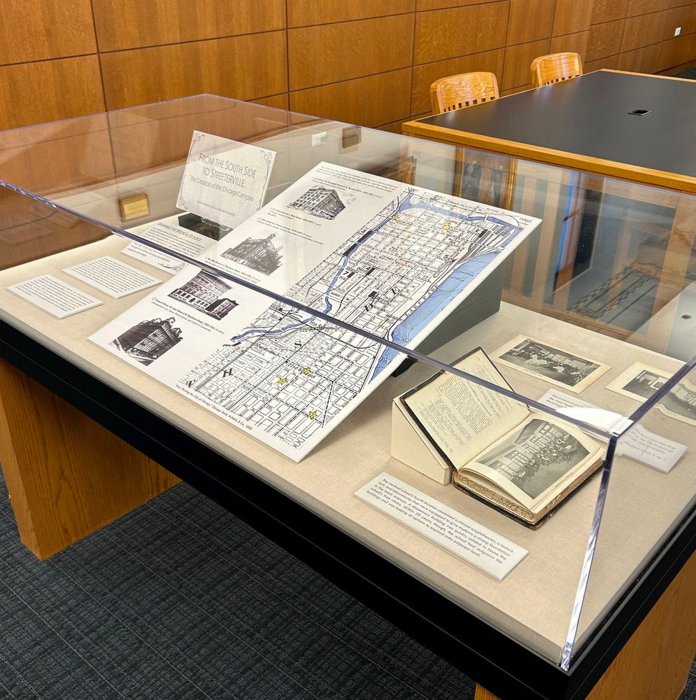 A display case in a library containing historical documents, including an old map, books, and printed text descriptions