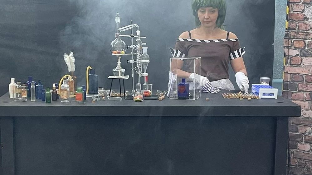 Oompa Loompa girl in Willy wonka scam event at her chem lab table 