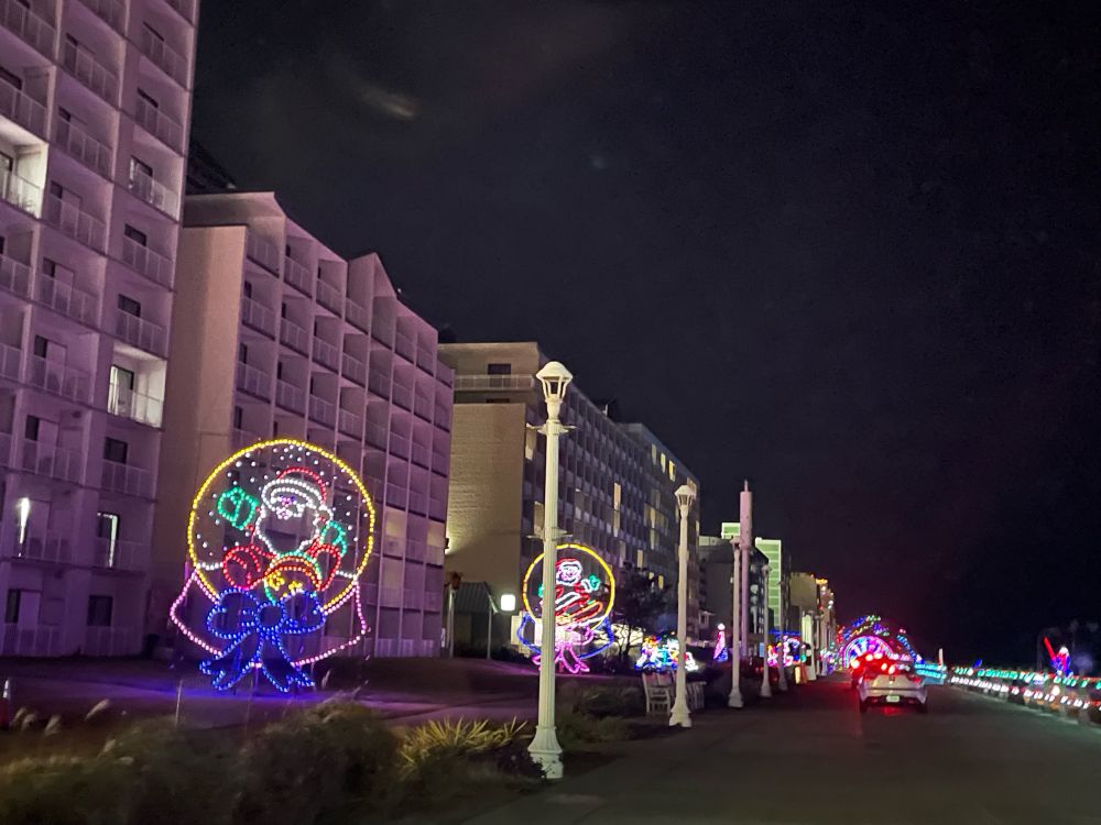 View of the drive through holiday lights on the Virginia Beach boardwalk. In the background hotels are visible and the displays of snow globes in front of the hotels