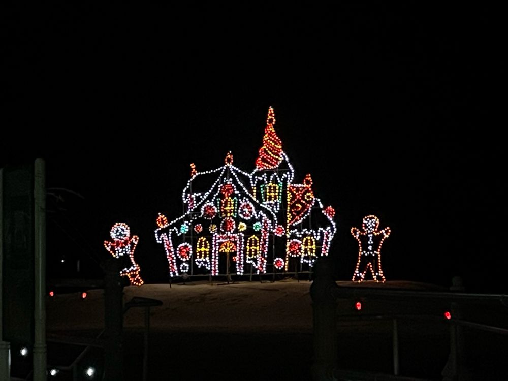 Drive through holiday light display of a decorative gingerbread house and gingerbread people on each side 