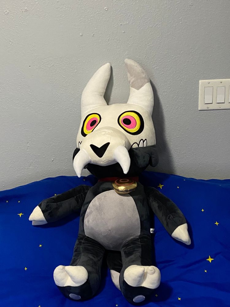 A giant plush of King from The Owl House sitting on top of a bed. The bed has a blanket with stars on it - though not visible, it's actually a Mario blanket.
