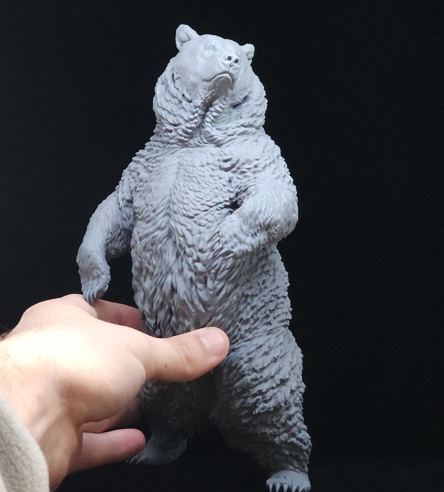 A sculpture I made of a grizzly bear, held in my hand. It is painted grey.