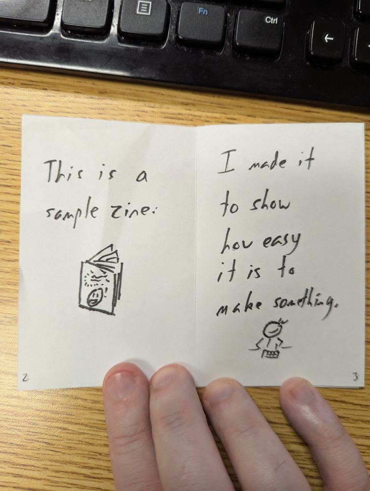 Photo of pages 2 and 3 of the zine. Page 2 has a picture of the zine and reads, "This is a sample zine." Page 3 has a stick figure doodle of me assembling the zine and reads "I made it to show how easy it is to make something."