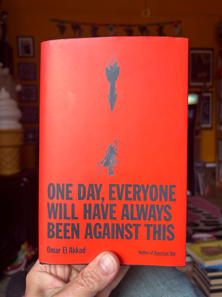 Holding up a copy of ONE DAY, EVERYONE WILL HAVE ALWAYS BEEN AGAINST THIS by Omar El Akkad