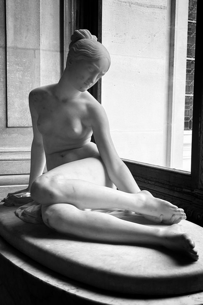 Femme assise, les jambes repliées sur le côté gauche. Son visage se tourne vers la gauche, derrière sa cuisse un scorpion est sculpté dans le socle de la statue.