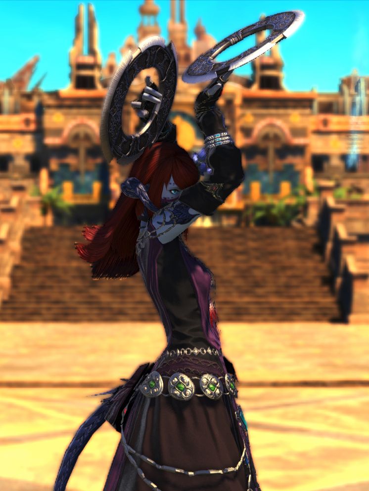 A blu-ish Au Ra with red hair and a black-purple dancer garb, dancing in front of the desert city of Rabanastre. Her face is partially hidden by her arms, which hold her chakrams towards the sky