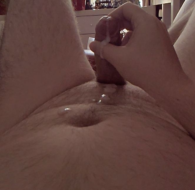 My erect penis, ejaculating. There are some splotches of cum on the stomach/pubis and a thick tail running over the thumb, which is stroking the top of the shaft and down the head/shaft of the cock itself