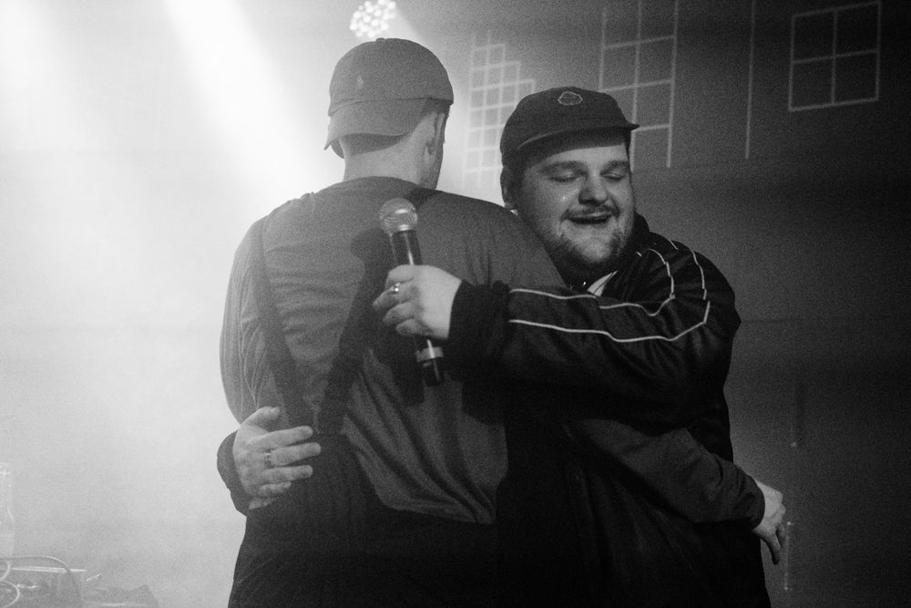 Zu sehen sind die deutschen Rapper MC Smook und Einfach Eddi auf einer Bühne. Sie umarmen sich.