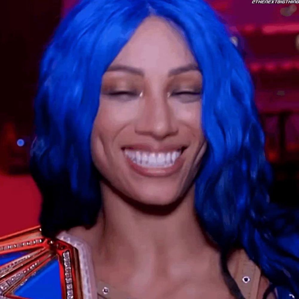 a woman with blue hair is smiling with her eyes closed and holding a championship belt .