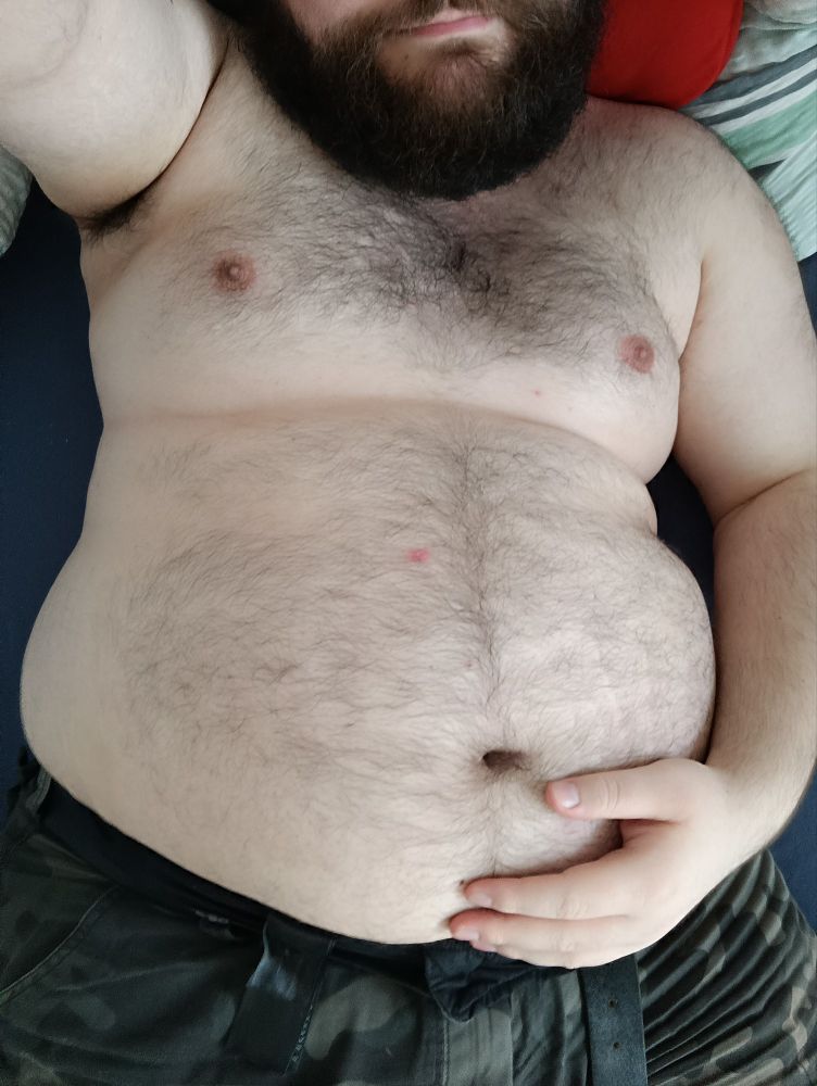 Bearded chubby guy showing off his belly lying in bed