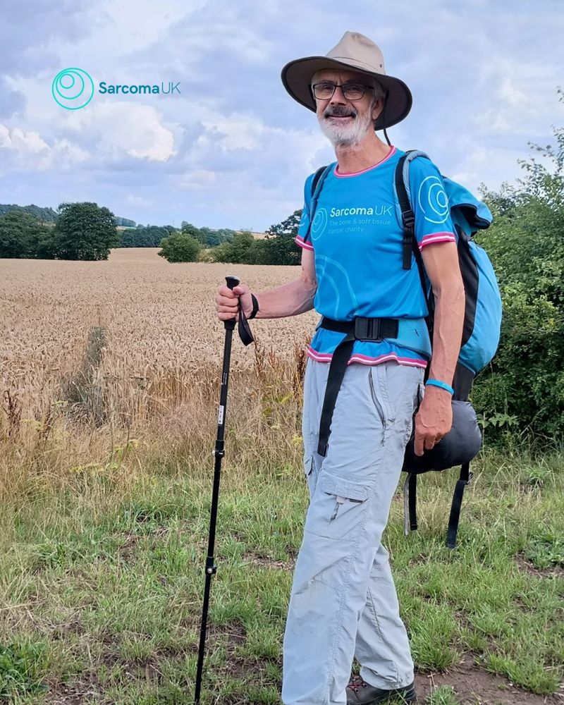 Photo of John in a Sarcoma UK top, walking in a field with a hiking stick.