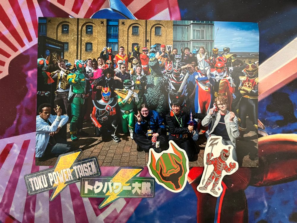 Photo of cosplayers and members of TokuPowerTaisen in the UK. Stickers of their logo in English and Japanese, MagiGreen Legend Helmet and Lord Zedd. 