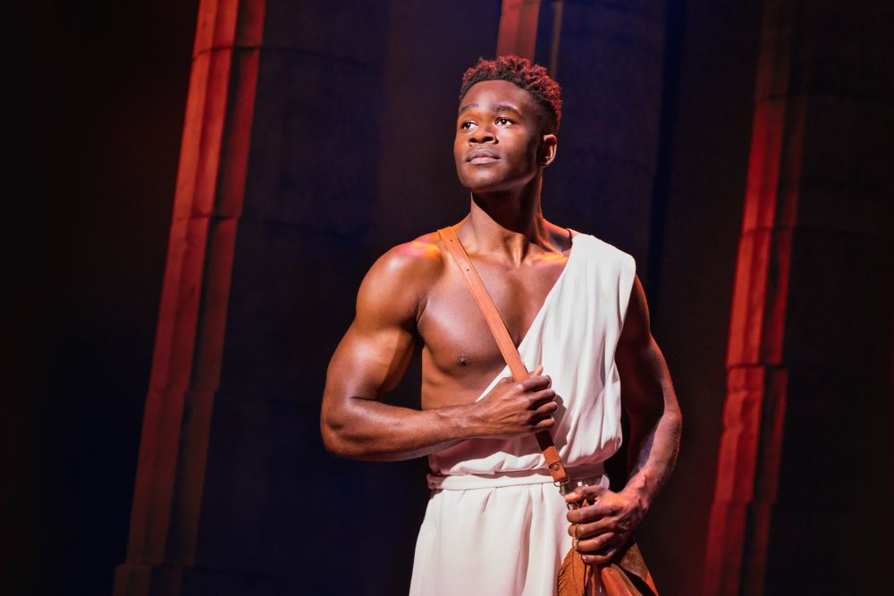Hercules is a Black man with a white outfit and dark oily hair with orange lighting.
