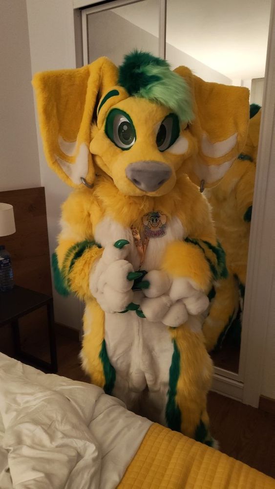 Anthropomorfic yellow and white dachshund with a lime green and dark green tuft looking at the camera with puppy eyes.