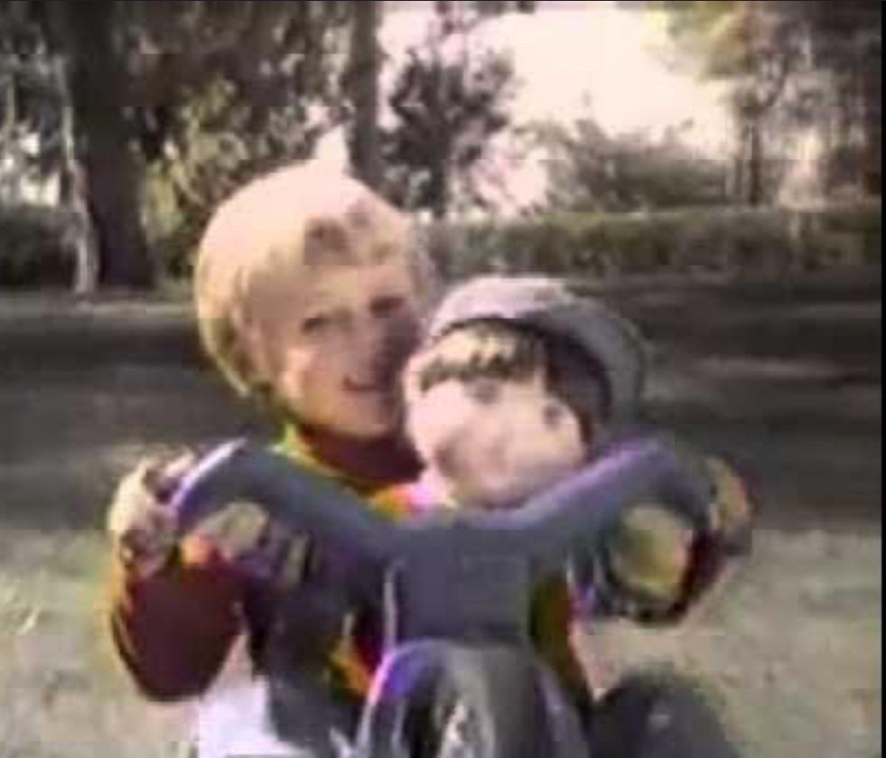 A still from the my buddy commercial, with the my buddy doll riding on a Big Wheel with a little boy. 