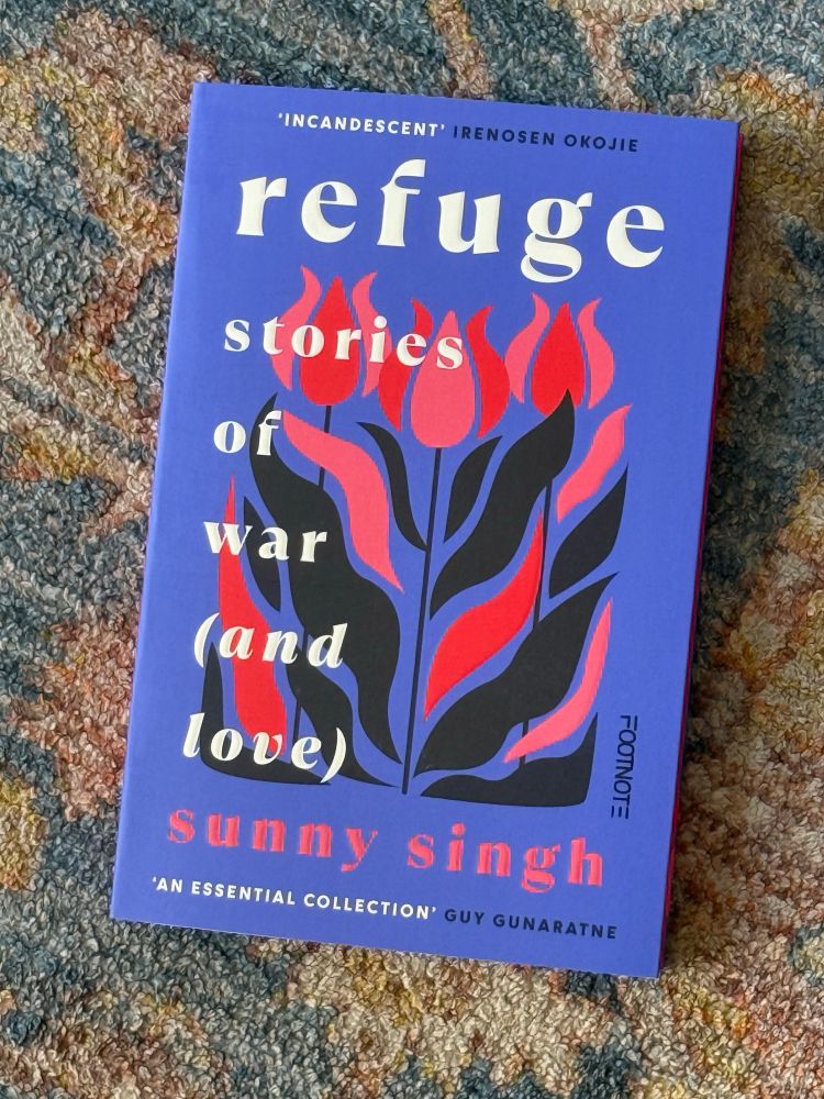 Book with purple background and white and black identifying text superimposed on red, pink and black flame like flowers placed on a multicoloured patterned background 