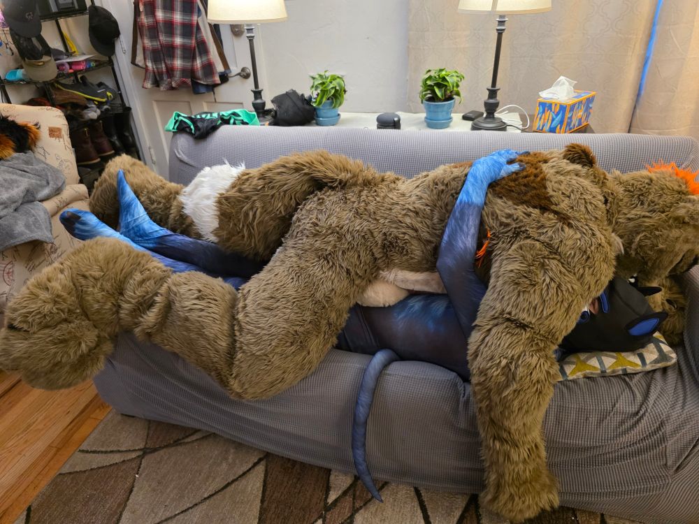 Arrow in fursuit laying on top of me while I'm in petsuit and pup hood, giving him a hug.