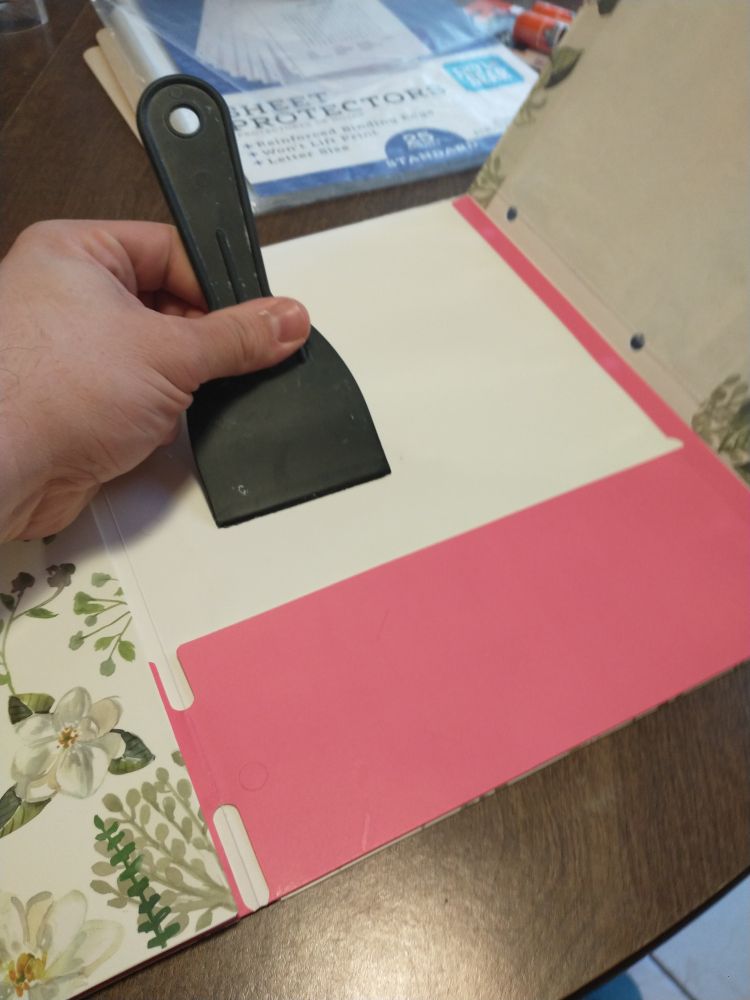 Folder being stuck together with glue, and a scraper being used to smooth and spread the glue.