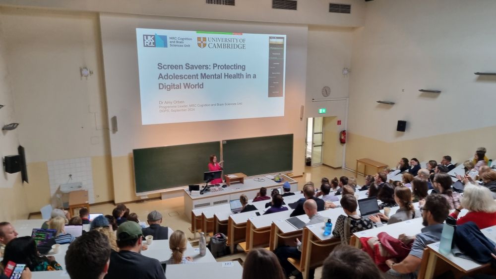 Lecture hall with filled seats  in the distant front, the speaker