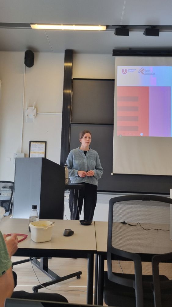 The presenter, a young women with brown hair, stands in front of the presentation screen