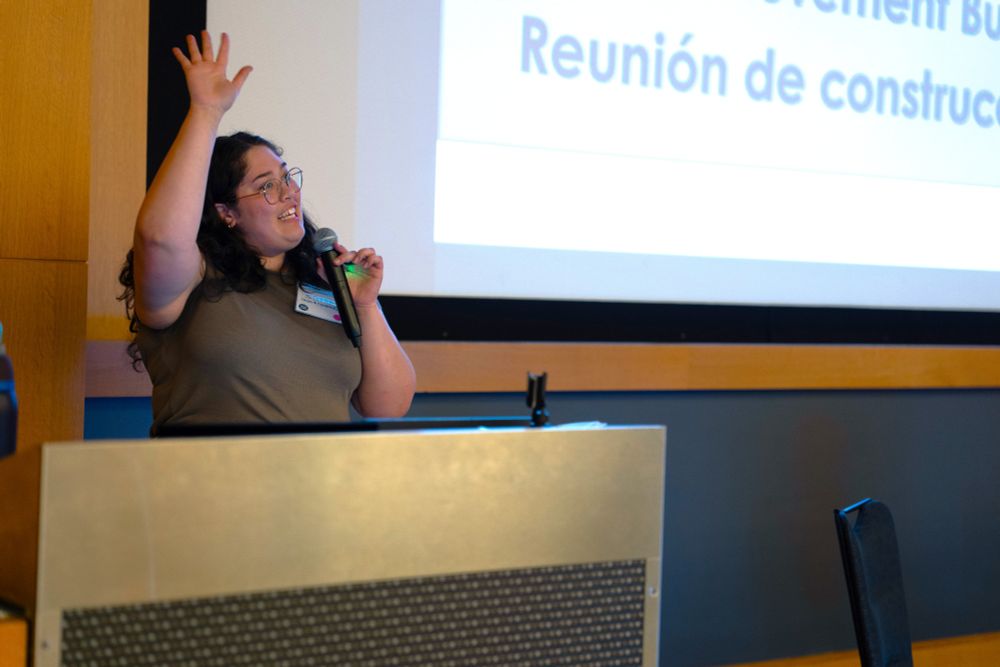 Cedarbrook Lodge, June 5, 2025 — A Front and Centered staff member smiles and raises their hand to greet the audience as they present from a podium.