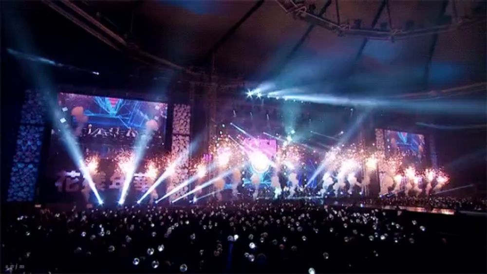 a crowd of people are gathered in front of a stage with fireworks and a screen that says ' bts ' on it