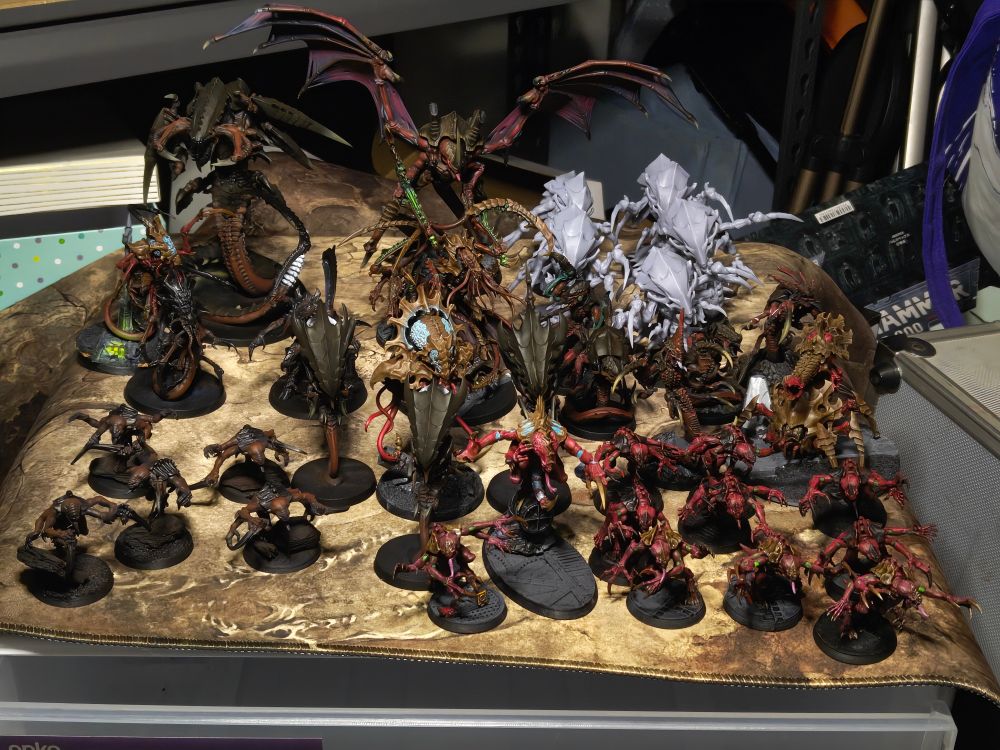 A tyranid army from Warhammer 40k sitting atop a tan brown marbled playmat.
Back row, left to right: Trygon prime, winged hive tyrant, both painted. Beside them is a group of 5 Hydralisks from StarCraft II that are unpainted grey printed resin.
Middle row, left to right: Two neurolictors, two lictors, Deathleapers, a neurotyrant and three zoanthropes, a unit of hyperadapted raveners and a biovore.
Front row, left to right: a unit of five genestealers, a Broodlord, and another unit of ten genestealers.