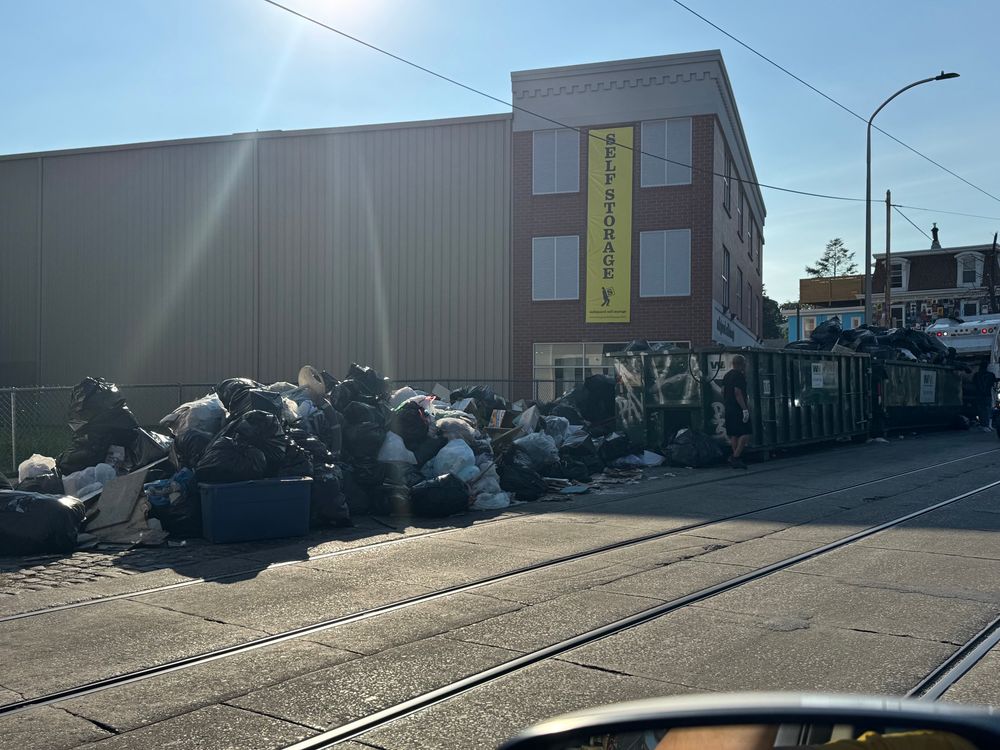A Belgian block street with trolley tracks down the middle. On the side of the street in one of the most historic neighborhoods in Philly is a mountain of trash