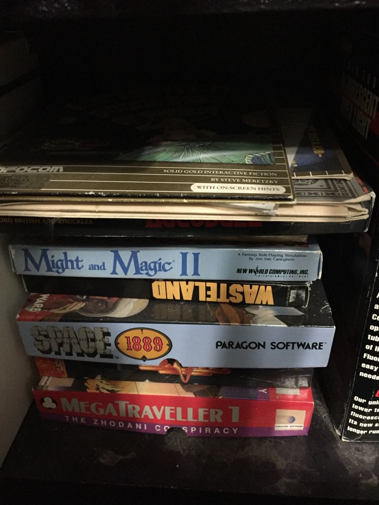 A stack of original boxes for PC Games. From top to bottom: Leather Goddess of Phobos, Planetfall, Might and Magic II, Wasteland, Space 1889, BAT, MegaTraveller 1. 