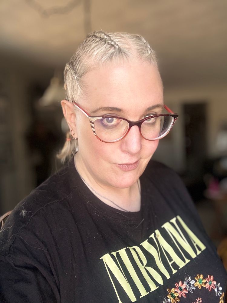 Danika looks forward her blonde hair is recently done into 4 rows of braids. Wearing a Nirvana T shirt with embroidered flowers forming a smiley face. She grins slightly with the anticipation that her surgery next week will be life changing.  