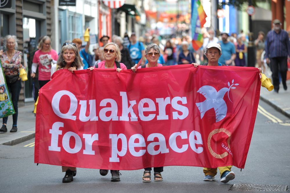 Four people march in a protest with a red banner reading - Quakers for peace.
