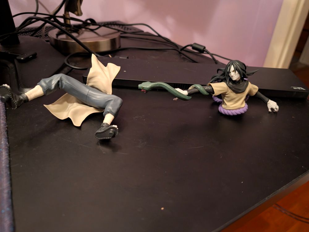 A figure of Orochimaru is disassembled on a black desk into the. There are two parts to the statue, the torso and the legs. 

This is a throwback to the time Orochimaru fought Four tailed beast cloak Naruto. 