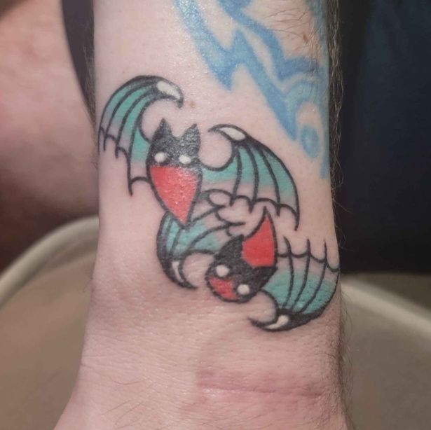 The finished tattoo of two bats, slightly overlapping as one flies up and the other down. Their bodies are droplet-shaped and gradient from black to red, with white dot eyes. The wings have little white claws on the tips and the membranes are a turquoise gradient/fade.