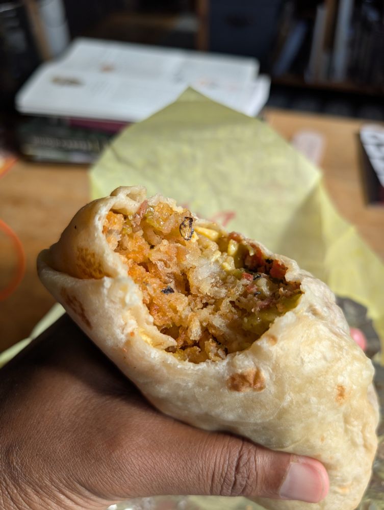 A photo of the breakfast burrito with a single bite taken out. You can see the hash browns, eggs, cheddar cheese, and bacon