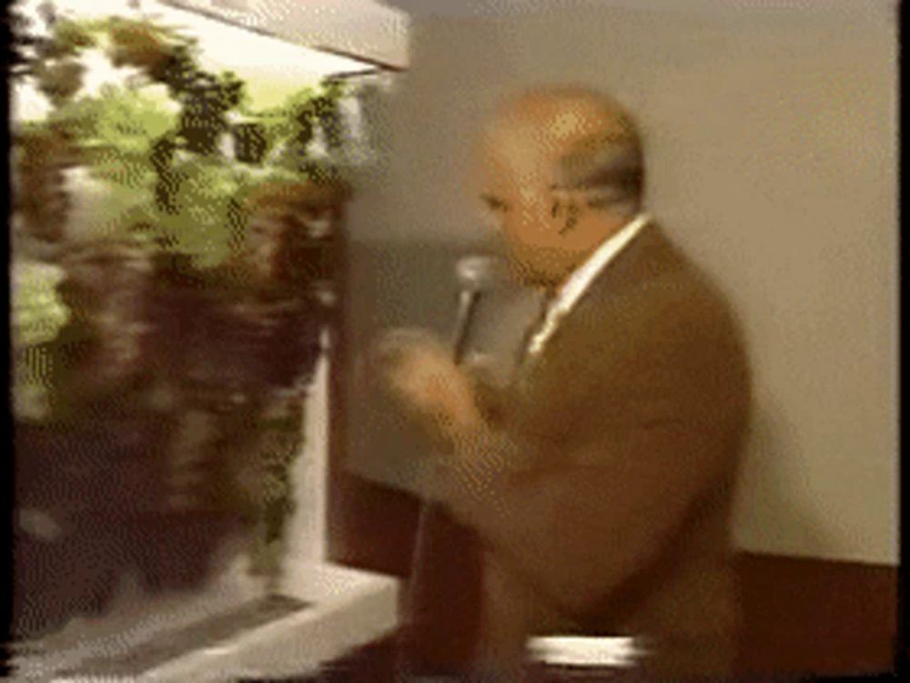 a man speaking into a microphone in front of a display of plants