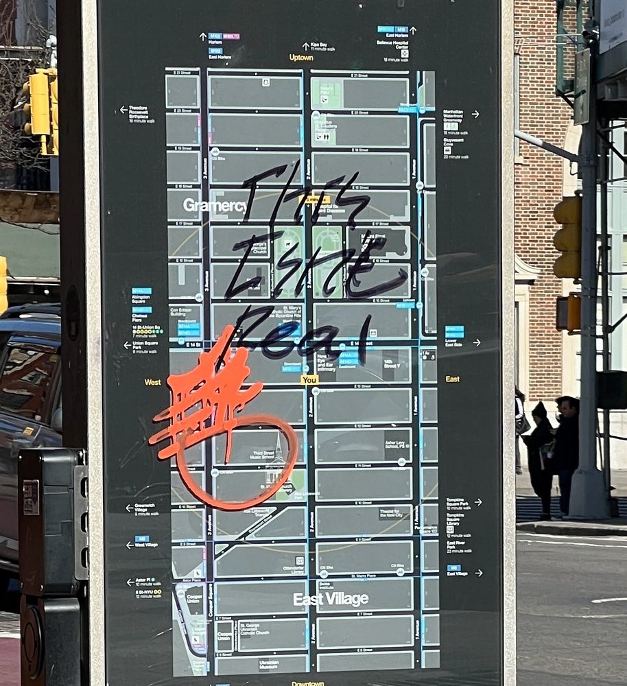 It’s a bus stop sign in New York with “this isn’t real” scrawled across the map