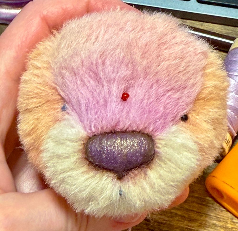 Small teddy bear head with ball-head pins marking the center of the face & eye placement. The nose is colored shifting and shimmery.
