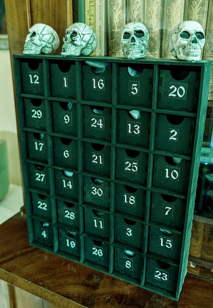 A wooden Halloween-themed "advent" calendar, but painted black with four small skulls on top, 